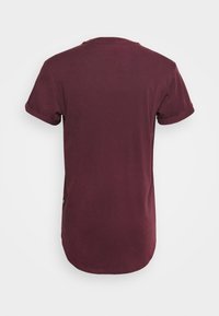 Bordowa koszulka z okrągłym dekoltem, krótkimi podwiniętymi rękawami i zaokrąglonym dołem; gładka struktura i minimalne detale brandingowe.