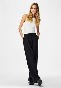 Pantalon noir à fines rayures avec une coupe décontractée, doté d'une taille à cordon de serrage et de poches latérales, assorti à un débardeur blanc côtelé.
