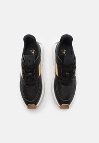 Sneaker nere con una parte superiore in pelle liscia, dettagli dorati e una suola bianca. Presentano forature e lacci neri.