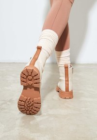 Kremowe botki za kostkę z teksturowaną gumową podeszwą, brązowymi akcentami i bocznym zamkiem. Żebrowane kremowe skarpetki zestawione z dopasowanymi legginsami.