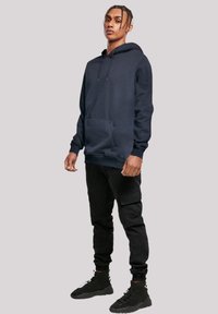 Navy blue hoodie made from soft fabric, featuring a front pocket, drawstring hood, and ribbed cuffs. Paired with black cargo pants and boots.