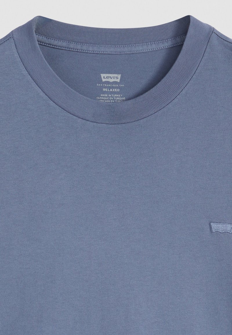 Camiseta azul de corte holgado, hecha de algodón, con cuello redondo acanalado y un pequeño logo bordado en la esquina inferior derecha.