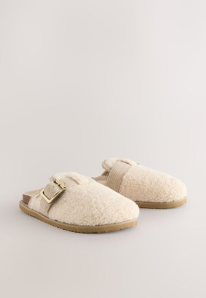 Pehmed kreemikad sussid, mis on valmistatud pehmest kangast, kaunistatud pannal ja elastse rihmaga. Iseloomulikult tekstureeritud pealmise osaga ja lame kummist tald.