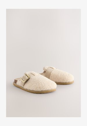 Pehmed kreemikad sussid, mis on valmistatud pehmest kangast, kaunistatud pannal ja elastse rihmaga. Iseloomulikult tekstureeritud pealmise osaga ja lame kummist tald.