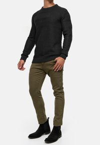Czarny sweter o fakturze dzianiny z okrągłym dekoltem, zestawiony z oliwkowozielonymi, dopasowanymi chinosami i czarnymi botkami za kostkę.