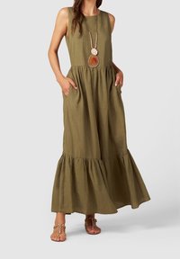 Oliwkowa, bezrękawnikowa sukienka maxi z dopasowanym gorsetem, falbaniastym dołem i kieszeniami. W zestawieniu z długim naszyjnikiem i płaskimi sandałami.