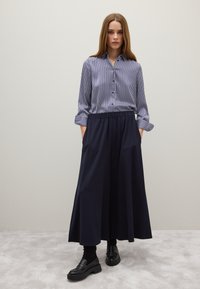 Camisa de botones a rayas en azul marino y blanco con mangas enrolladas, combinada con una falda larga azul marino con cinturilla elástica y bolsillos laterales.