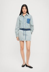 Denim jaka ar zilu kabatu, īsāko dizainu, gaiši zilu krāsu, garām piedurknēm un svārkiem ar elastīgu jostu no līdzīga auduma. Melnas dzīvokļu kurpes.