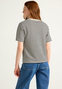 Gestreiftes T-Shirt in Schwarz und Beige, mit kurzen Ärmeln und lockerer Passform. Kombiniert mit hoch taillierten blauen Jeans.