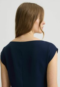 Tengerészkék dressz széles nyakkal és rövid ujjakkal, sima textúrával és finom varrással a hátsó részen.