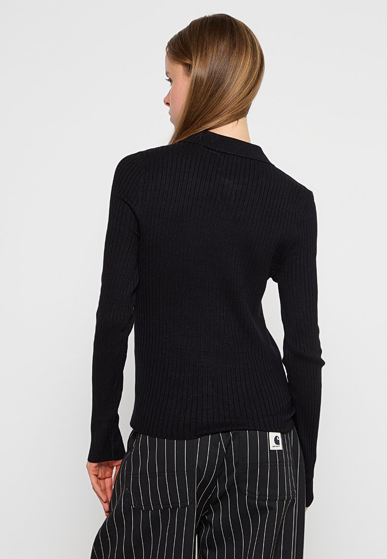 Maglietta nera a maniche lunghe con righe, dal design aderente e colletto, abbinata a pantaloni neri a righe con un patch logo sul retro.