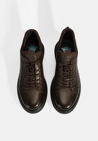 Braune Lederschuhe mit runden Zehen, texturierten Oberflächen, Schnürung und kontrastierenden schwarzen Gummisohlen. Das Label "DESA COMFORT" ist auf den Zungen sichtbar.