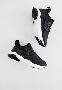 Para czarno-białych sneakersów sportowych z grubymi podeszwami i siateczkowymi detalami na jasnoszarym tle.