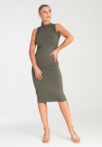 Oliwkowa midi sukienka bez rękawów z miękkiego, rozciągliwego materiału o wysokim kołnierzu. Charakteryzuje się dopasowanym krojem i płaskimi szwami. Przezroczyste strap heels.