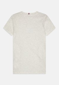 Světlé šedé bavlněné tričko s kulatým výstřihem. Krátké rukávy, klasický střih a malý trojbarevný akcent na zadní straně u krku.