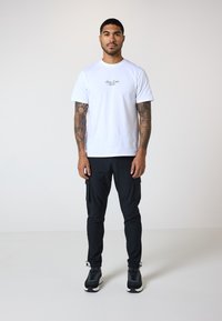 Hvid bomulds T-shirt med trykt logo, parret med sorte cargo bukser med sidelommer og sorte sneakers med struktureret design.