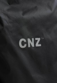 Zwarte stof met een matte textuur en een prominent, reflecterend wit "CNZ™" logo gedrukt in het midden.