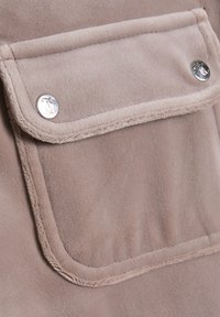 Beige stof met een gladde textuur, voorzien van een klepzak die wordt bevestigd door twee zilveren drukknoopjes. Stiksels zijn zichtbaar langs de randen.