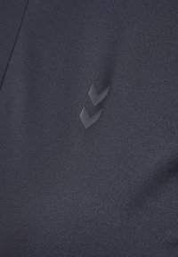 Marinblå idrottstyg med en mjuk textur och en subtil lyster, prytt med en liten präglad logotyp av två chevronger.