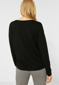 Top nero a maniche lunghe con vestibilità morbida, scollo ampio e texture morbida, abbinato a pantaloni a quadri neri e bianchi.