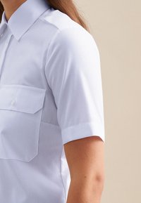 Camicia a maniche corte con bottoni in tessuto bianco, caratterizzata da colletto, due tasche sul petto e tessuto liscio. Elementi di design puliti e classici.