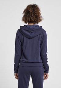 Mörkblå hoodie med en texturerad yta, som har en rymlig huva och vita accentlinjer längs ärmarna. Designad för komfort och passform.
