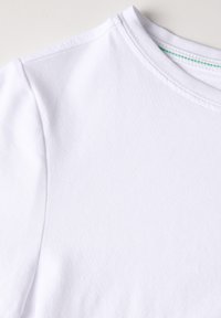 T-shirt en coton blanc avec un encolure arrondie, présentant une texture lisse et une couture verte subtile le long du col.