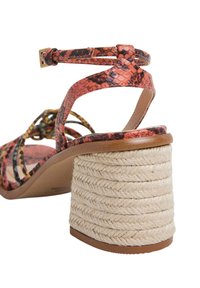 Strappy High-Heel-Sandal mit einem lebhaften orangefarbenen Schlangenleder-Obermaterial, ausgestattet mit einem gewickelten Seilabsatz und einer glatten, sandfarbenen Sohle.