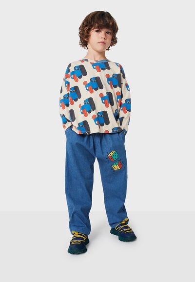 Camisa de manga larga color crema con estampado de vehículos multicolores, combinada con pantalones de mezclilla azules que tienen un gráfico de dados, y calzada con zapatos multicolores.