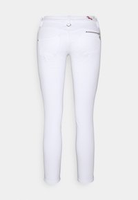 Jeans ajustados blancos con un diseño clásico, acentos de bolsillos traseros con cremallera y una textura de denim suave.