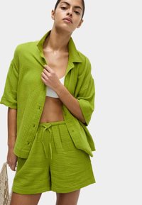 Completo a due pezzi in cotone testurizzato di colore verde lime, composto da una camicia loose con bottoni e pantaloni corti con coulisse, dal taglio rilassato e design casual.