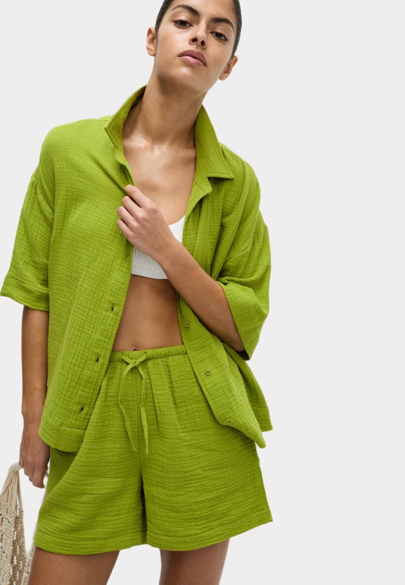Completo a due pezzi in cotone testurizzato di colore verde lime, composto da una camicia loose con bottoni e pantaloni corti con coulisse, dal taglio rilassato e design casual.