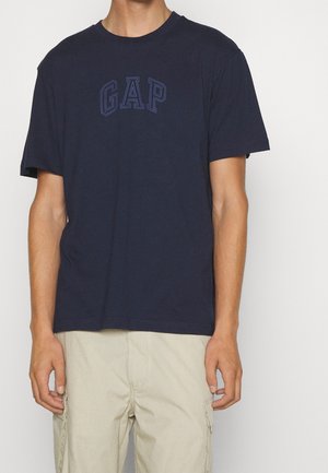 Marineblaues Baumwoll-T-Shirt mit kurzen Ärmeln, rundem Ausschnitt und dem in Dunkelblau geprägten Schriftzug "GAP" auf der Brust.