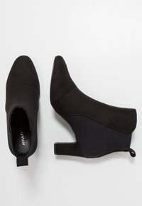 Bottines noires à bout pointu, dessus en daim lisse, panneaux latéraux élastiques et petit talon bloc. Comprend une languette pour faciliter l'enfilage.