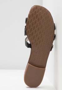 Schwarze Sandale mit einer strukturierten braunen Sohle, die ein graviertes Muster aufweist. Sie verfügt über verstellbare Riemen für einen sicheren Sitz.