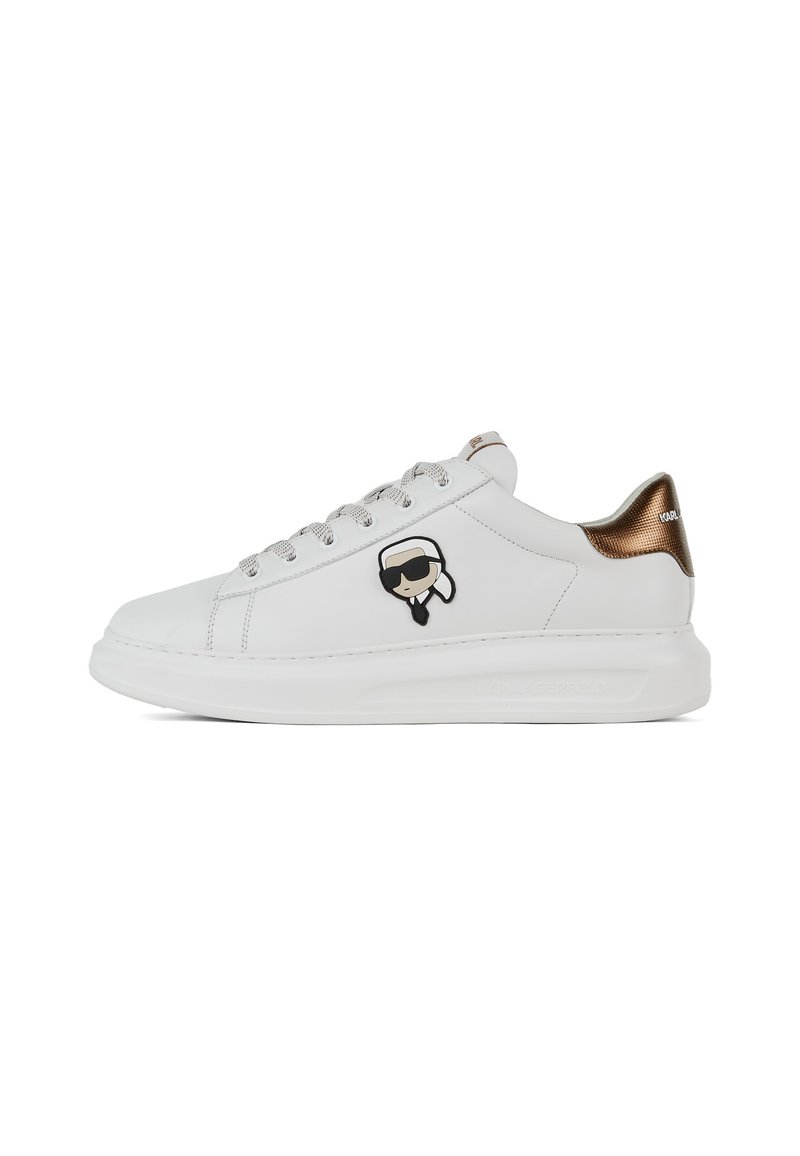 Sneaker in pelle bianca con un accento in pelle lucida marrone sul tallone, lacci argentati e un logo di carattere nero sul lato. Suola arrotondata e texturizzata.