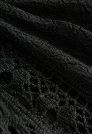 Schwarzer strukturierten Stoff mit einem erhabenen Muster und offenen Spitzenakzenten. Verfügt über ein zerknittertes Design und eine variierte Oberflächentiefe. Weich und gemustert.