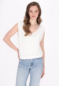 Løs pasform hvid ærmeløs top med V-hals og elastisk talje, parret med lys blå denimjeans. Glat stoftekstur, minimal design.