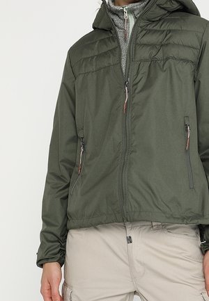 Person trägt eine olivgrüne Kapuzenjacke mit Frontreißverschluss und Reißverschlusstaschen, kombiniert mit hellbeigen Cargo-Hosen.