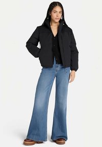 Czarna pikowana kurtka z wysokim kołnierzem, zestawiona z szerokimi dżinsami o luźnych nogawkach w kolorze niebieskim. Kurtka wykonana jest z gładkiej tkaniny i ma krótki fason.