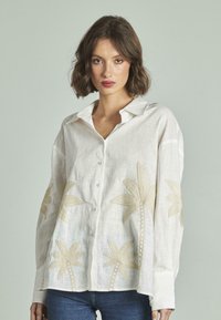 Blusa in lino di colore avorio, con ricami dorati a forma di palma. Design con bottoni, maniche lunghe e colletto classico.