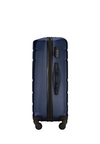 Valigia rigida blu navy con finitura testurizzata, manico laterale e doppia cerniera, poggiata su quattro ruote nere per una facile mobilità.