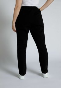 Zwarte, aansluitende sweatpants met een elastische tailleband, een soepele textuur en taps toelopende pijpen. Dragen met witte sneakers, die een eenvoudig ontwerp laten zien.