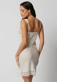 Vestido de pala con encaje en suave tela color crema. Presenta una silueta ajustada, tirantes ajustables y detalles de encaje floral en el corpiño y el dobladillo.