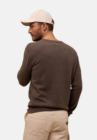 Hnědý vlněný svetr s kulatým výstřihem, žebrovanými manžetami a lemem, spárovaný s béžovými kalhotami s zadními kapsami a zeleným logem.