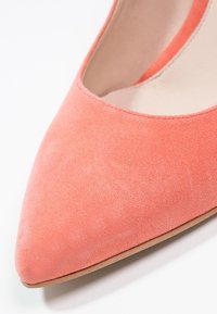 Chaussure plate en daim rose corail à bout pointu, montrant l'avant et une partie de la doublure intérieure sur fond blanc.