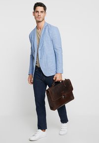 Lyseblå, skræddersyet blazer over en beige t-shirt, parret med mørke denimjeans. Holder en mørkebrun lædertaske med en lås. Hvide sneakers.