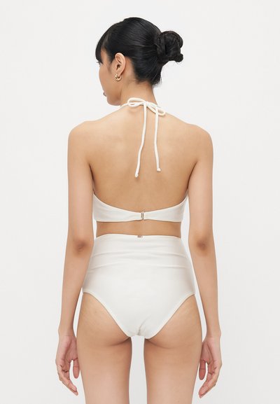 Costumul de baie alb constă dintr-un top halter cu închidere prin legare și o pereche de chiloți cu talie înaltă, ambele dintr-un material neted și elastic.