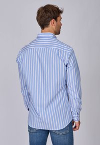 Chemise à manches longues rayée bleu et blanc avec poignets à bouton, affichée de dos, présentant un ourlet arrondi.