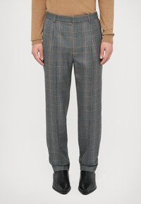 Pantalons à carreaux gris avec des accents orange et bleu, présentant une coupe droite, des plis et une taille classique, associés à des chaussures noires.